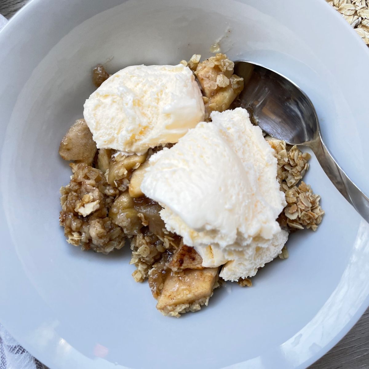 close up of apple crisp in white bowl with ice cream and spoon