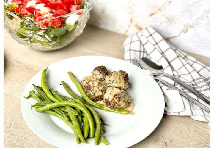 Easy low carb Swedish meatballs in cream sauce on plate with green beans and salad