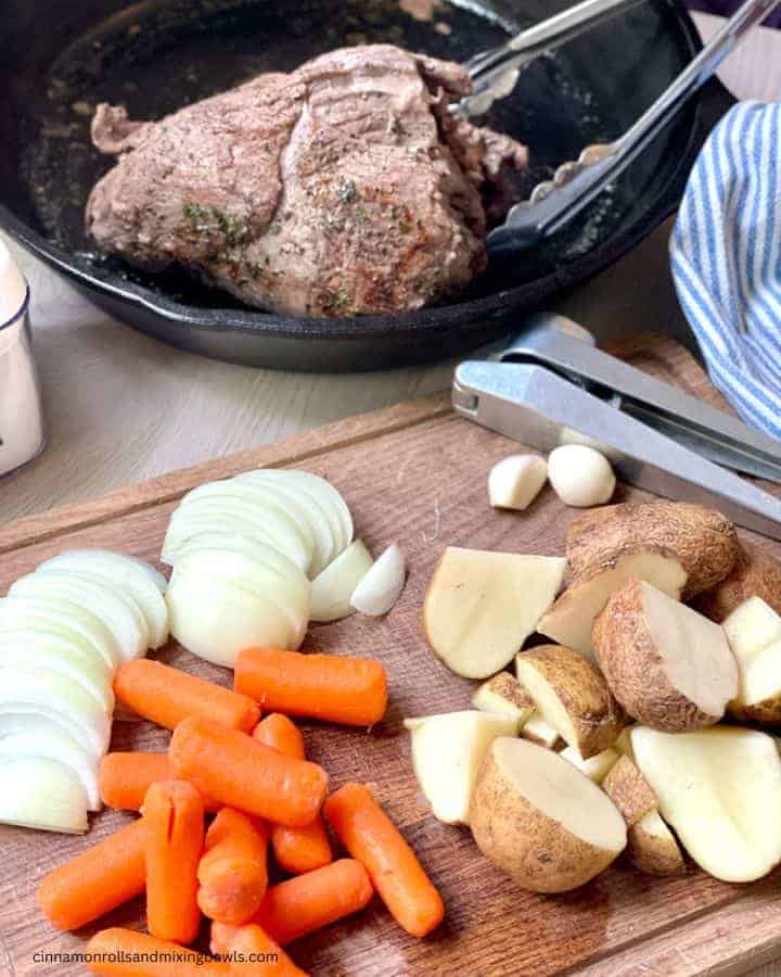 tender venison roast in the crockpot with gravy next to vegetables 