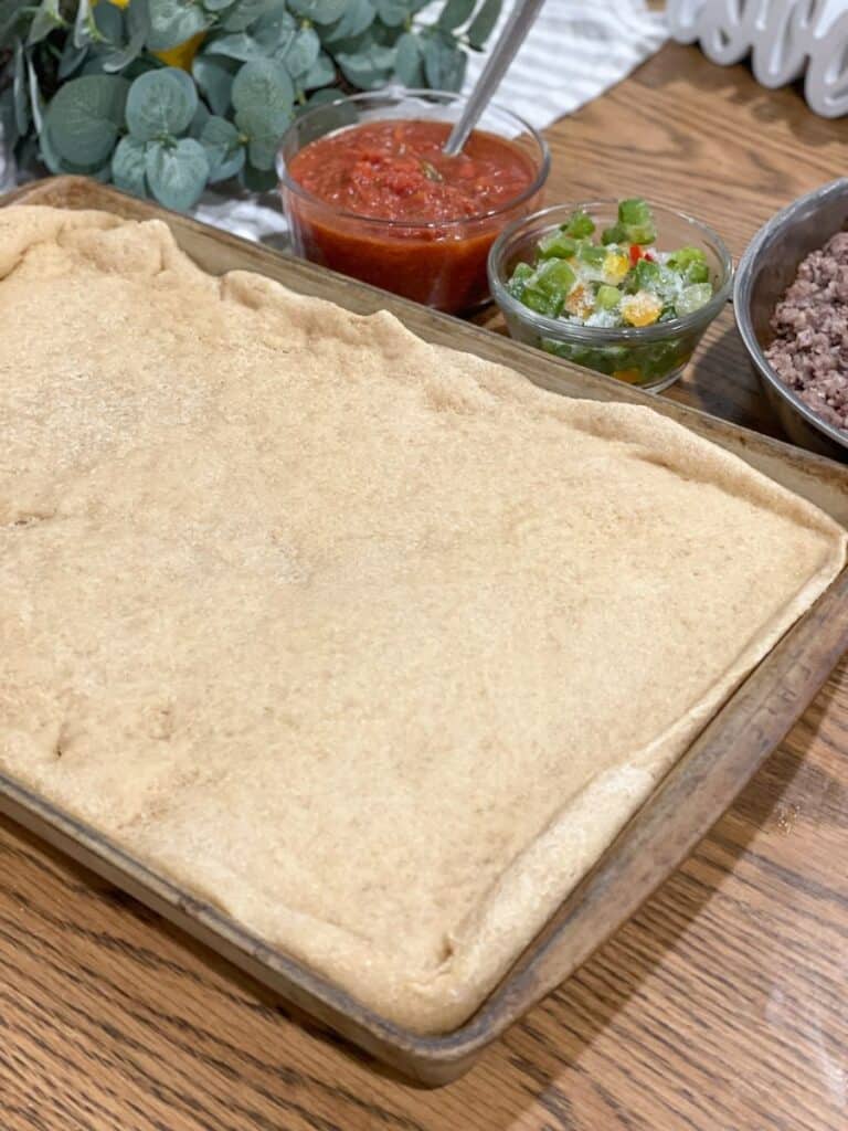 pizza crust par baked in pan next to toppings 
