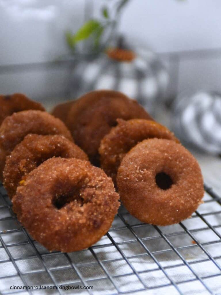 freshly milled pumpkin cake donuts lined up on cooling rack under window